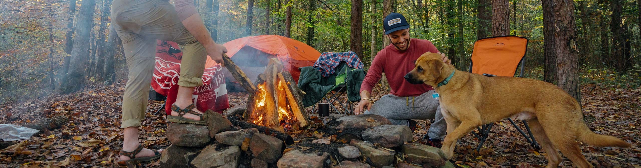 two men and a dog building a fire while camping