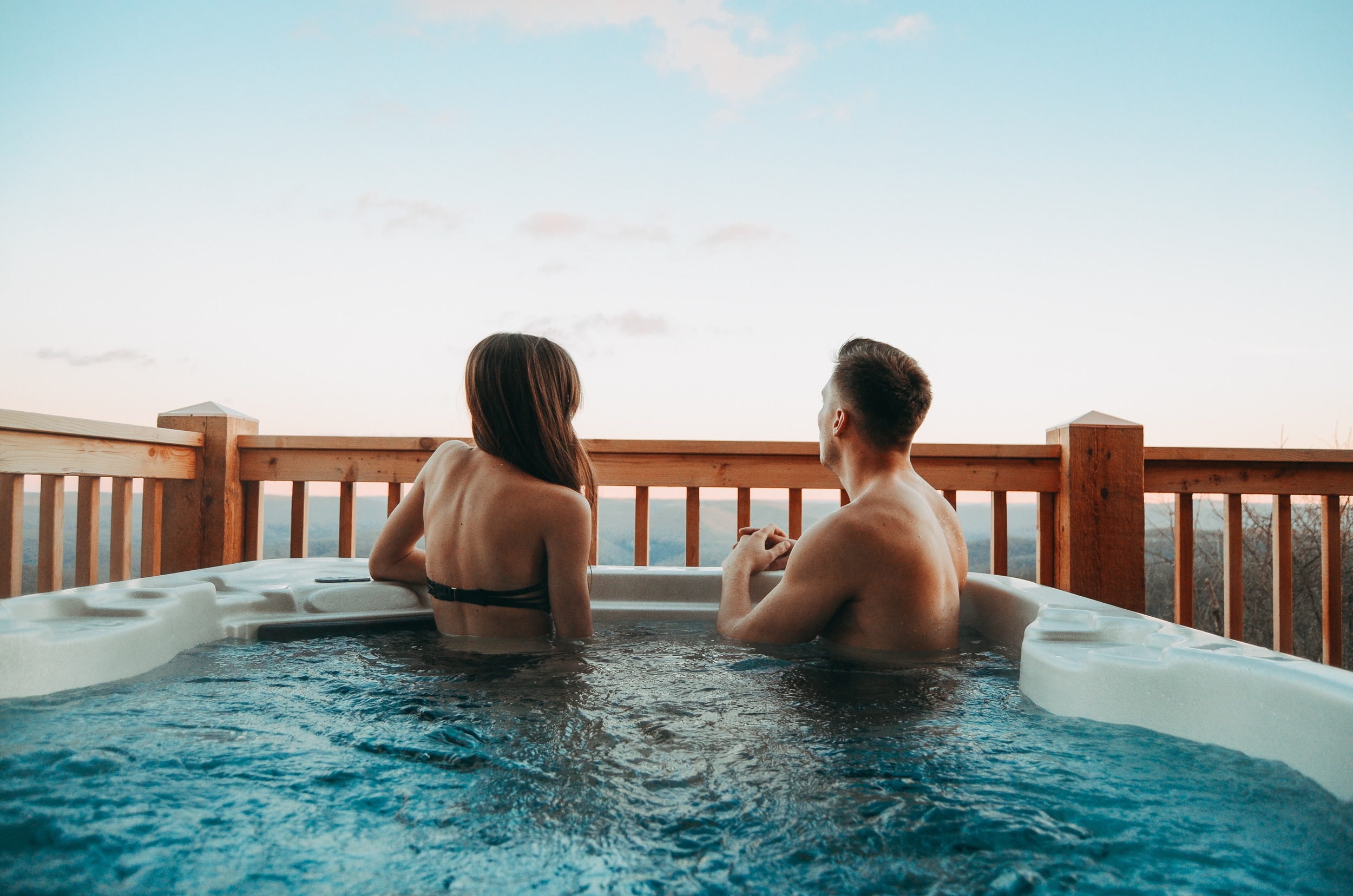 A couple in a hot tub located on a cabin deck overlooking Ozark mountains